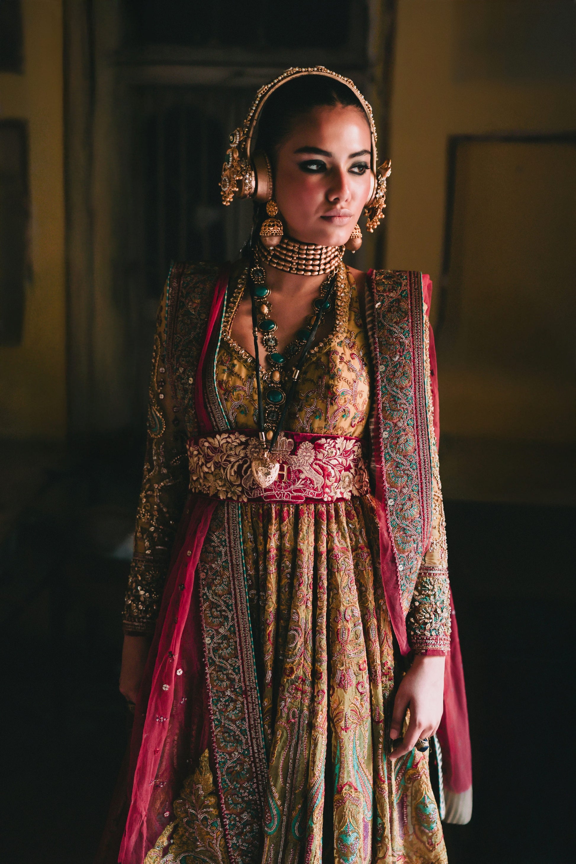 Woman in traditional attire with intricate patterns and jewelry in a dimly lit setting