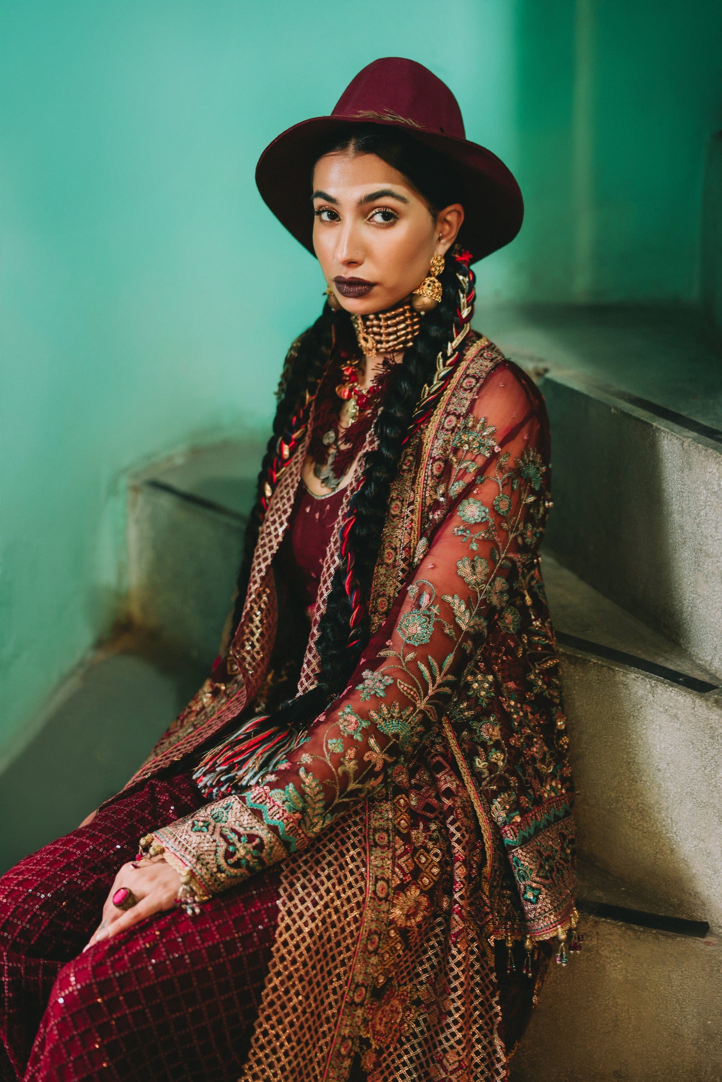 Woman in a patterned outfit sitting on steps with a teal wall background