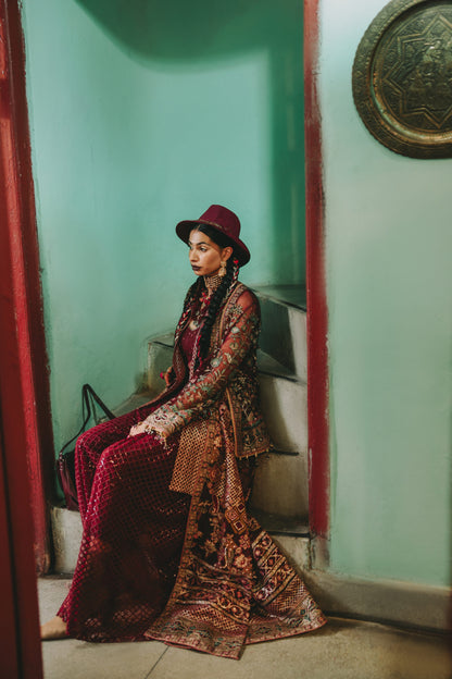 Woman in traditional attire sitting in a doorway with a green wall and decorative plate.