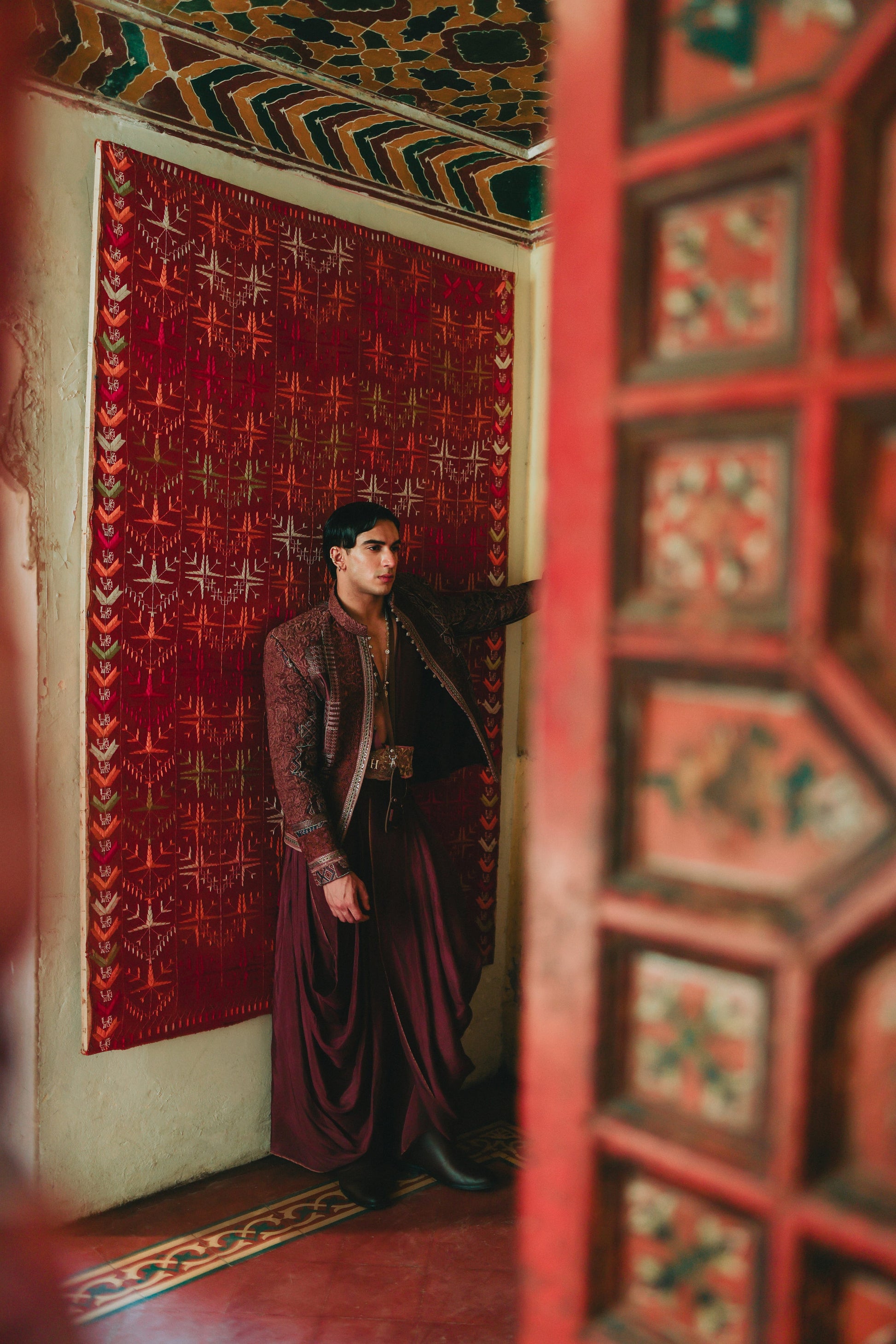 Person in a burgundy outfit standing in a room with ornate red walls and ceiling.