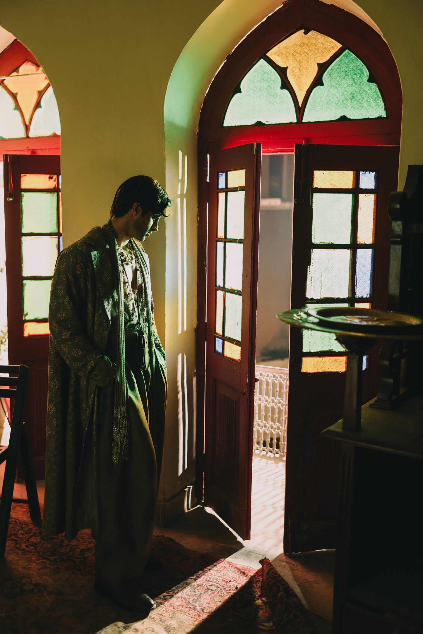 Person standing in a room with stained glass windows and a door open to a garden.