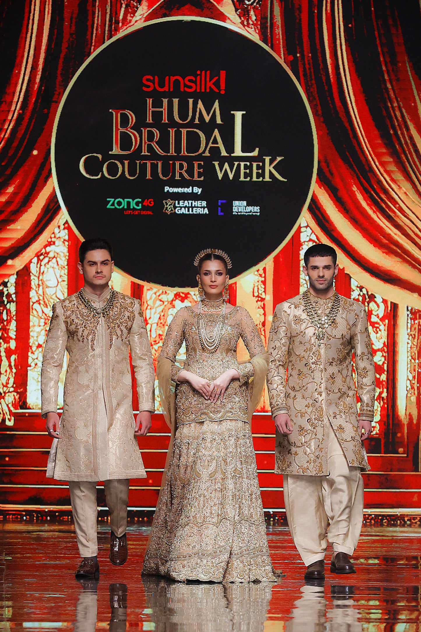 Three models in formal attire on a stage with 'Sunsilk Hum Bridal Couture Week' backdrop.