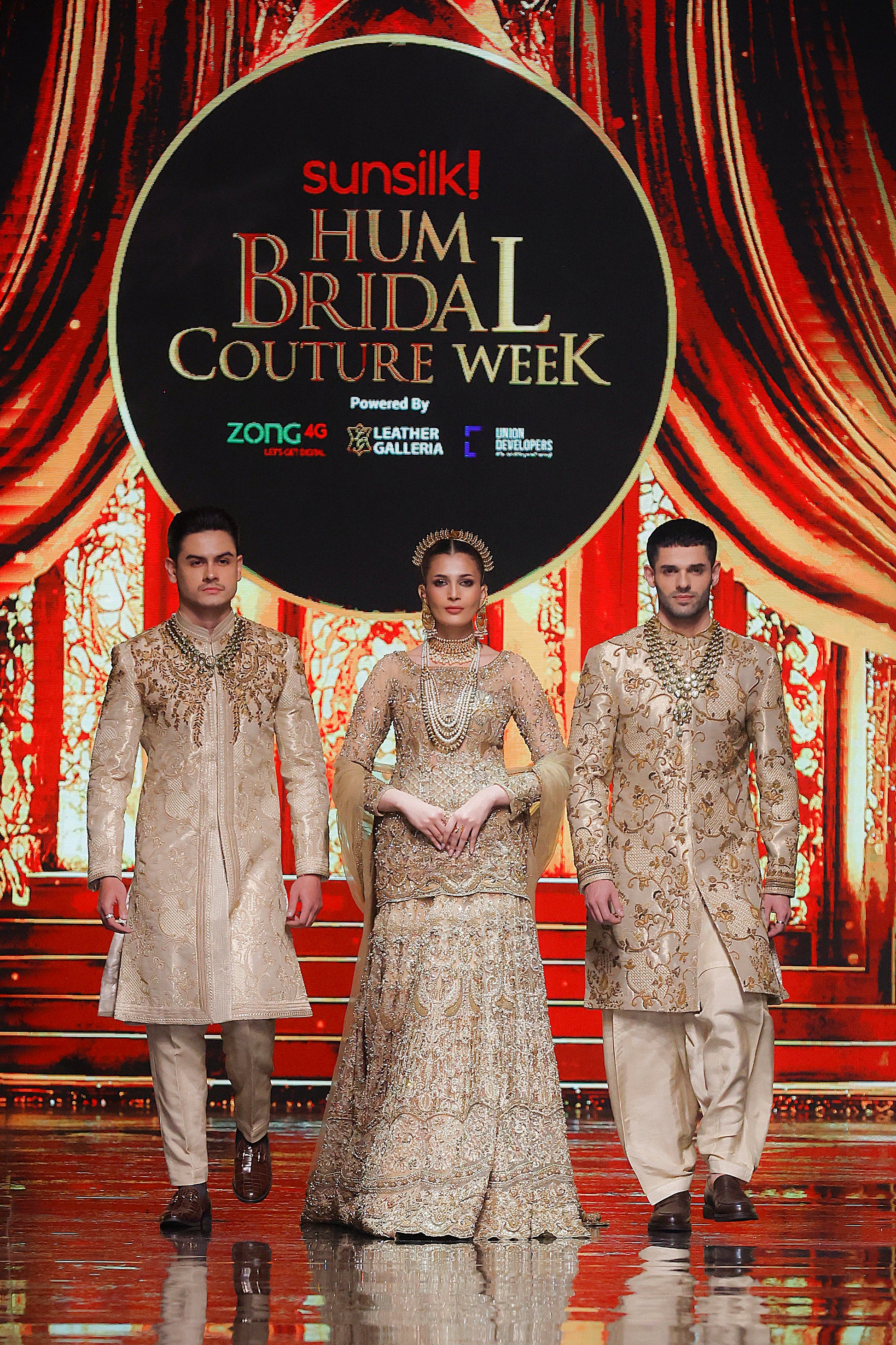 Three models in formal attire on a stage with 'Sunsilk Hum Bridal Couture Week' backdrop.