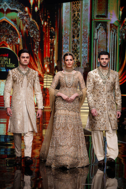 Two men and a woman in formal attire on a stage with decorative background