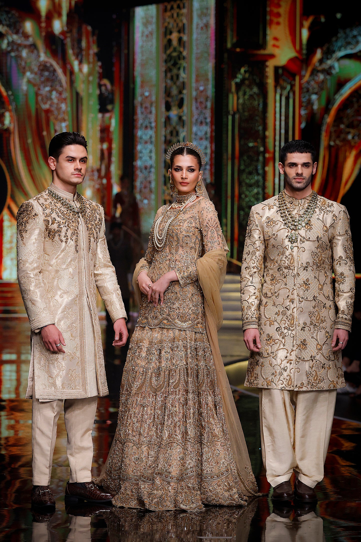 Three models in traditional embroidered outfits on a stage with decorative background