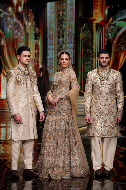 Three models in traditional embroidered outfits on a stage with decorative background