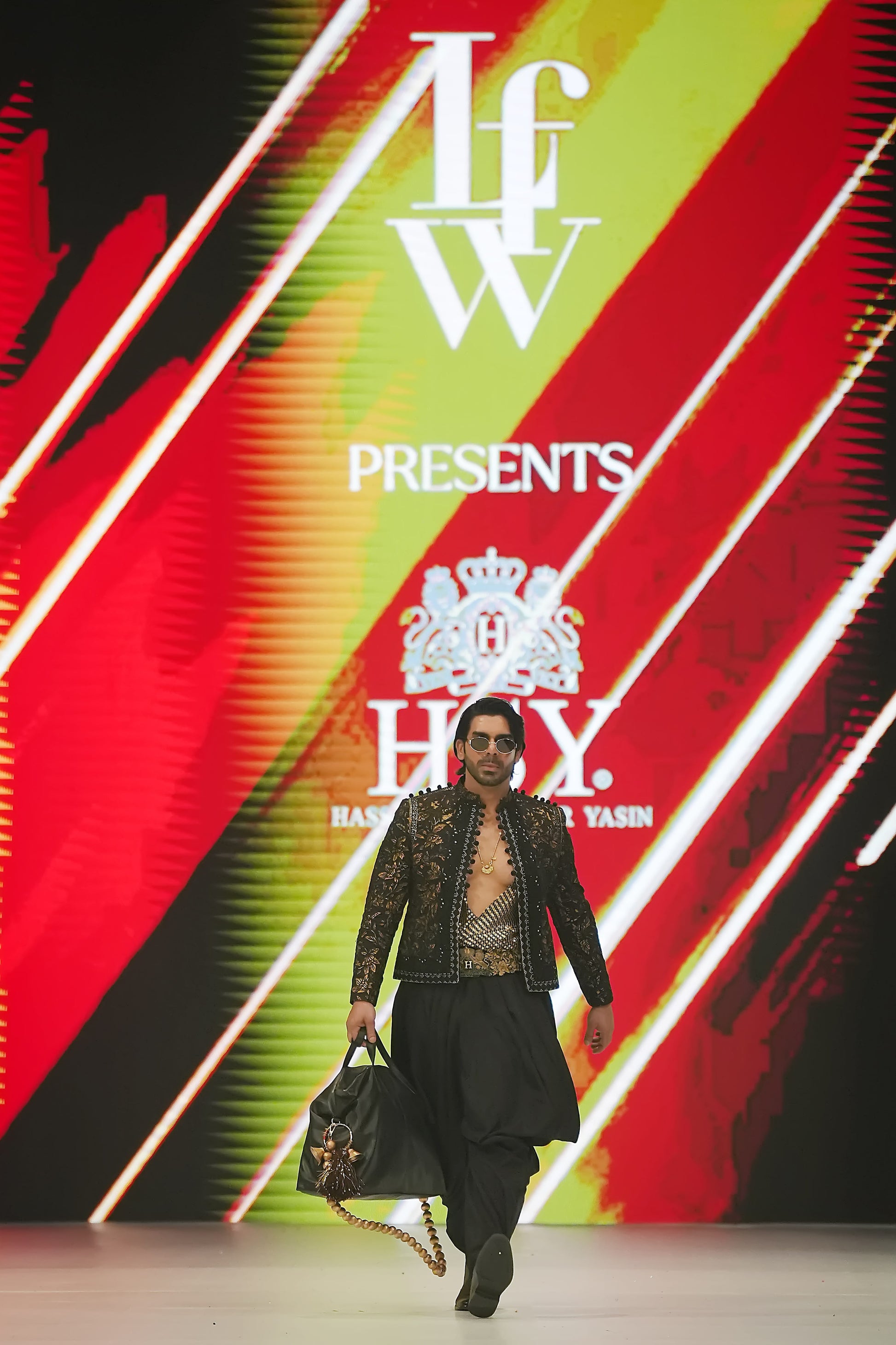 Model walking on a catwalk with a colorful background featuring 'IFW' and 'Hsy' logos.
