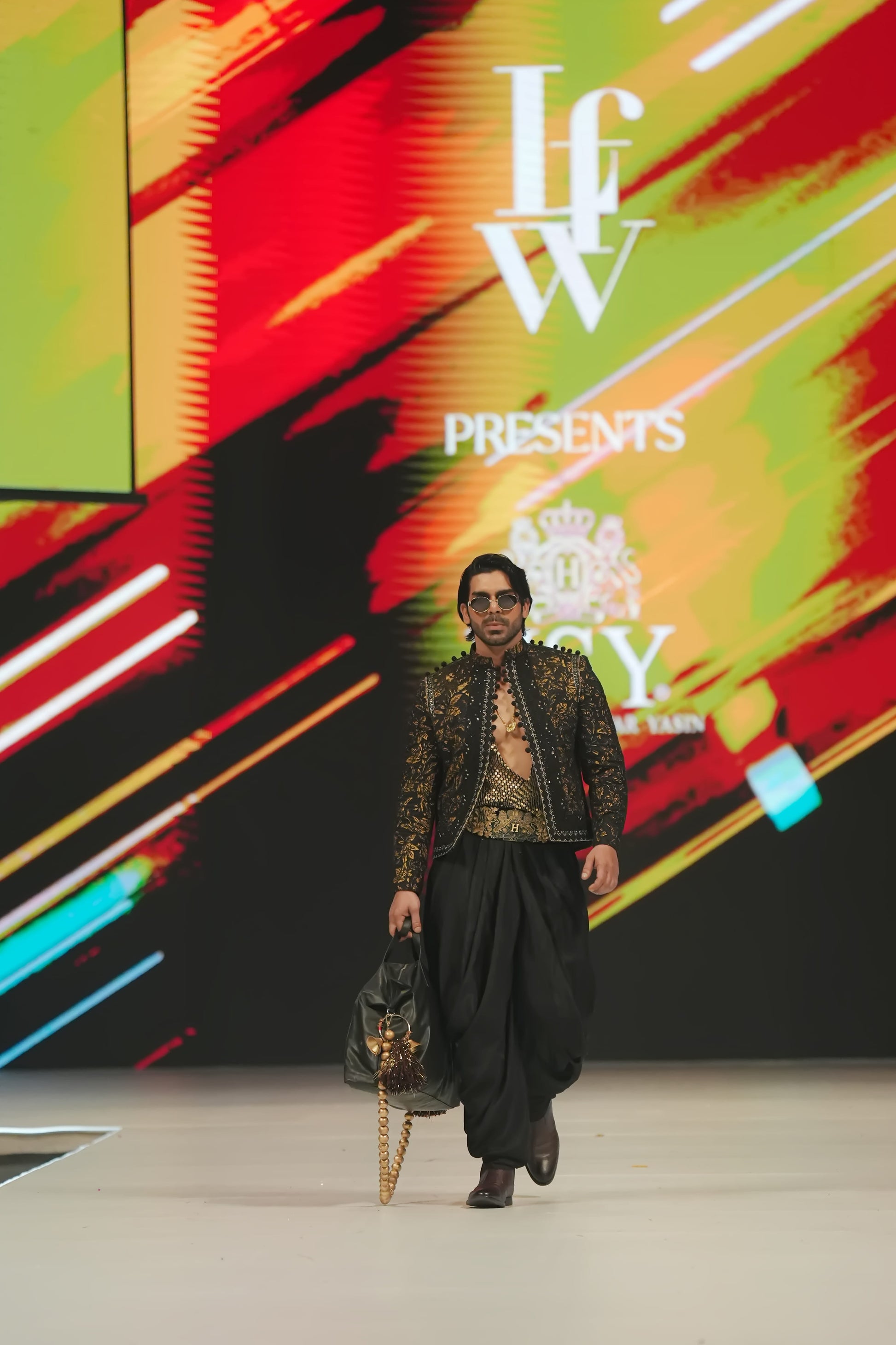 Model walking on a catwalk with a colorful background displaying 'IFW Presents'.