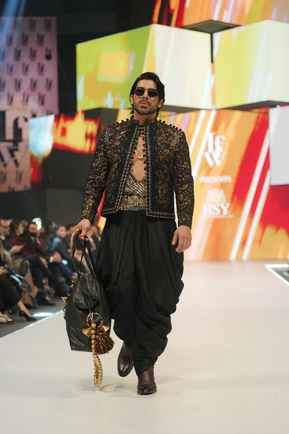 Man walking on a fashion show runway wearing a detailed outfit with a colorful backdrop.