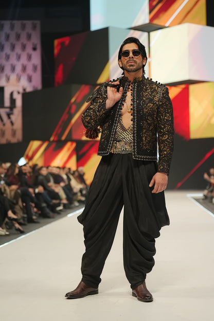 Man modeling a traditional outfit on a fashion show runway with a colorful background.