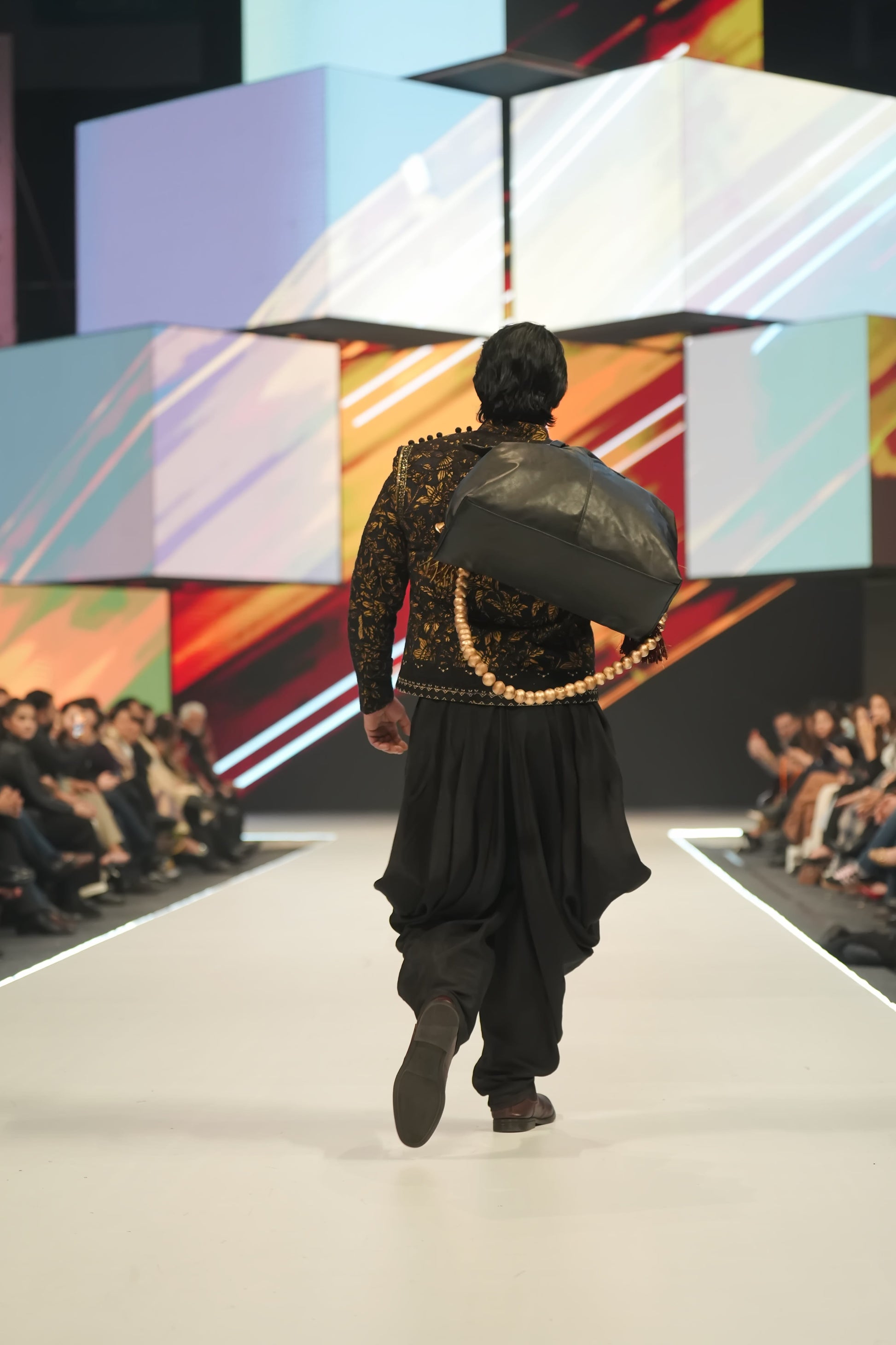 Model walking on a fashion show runway with colorful geometric background