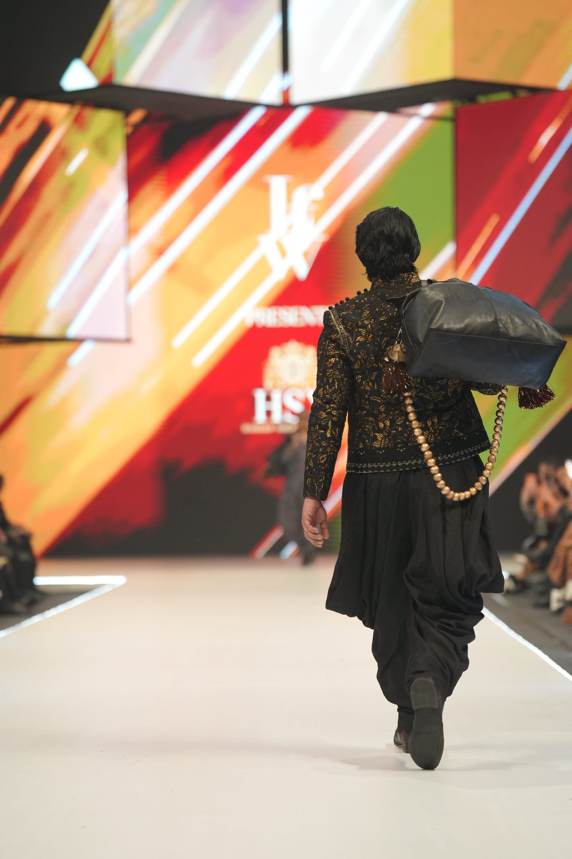 Model walking on a fashion show runway with a colorful backdrop