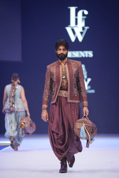 Man walking on a runway wearing traditional attire with 'IFW' branding in the background.
