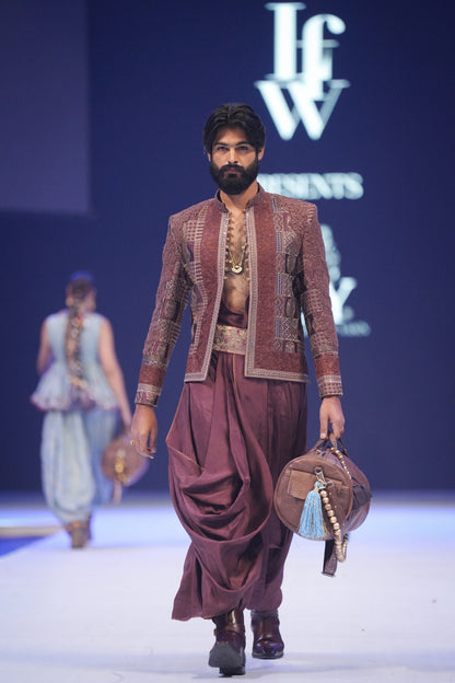 Man walking on a fashion show runway wearing traditional attire with 'IfW' branding in the background.