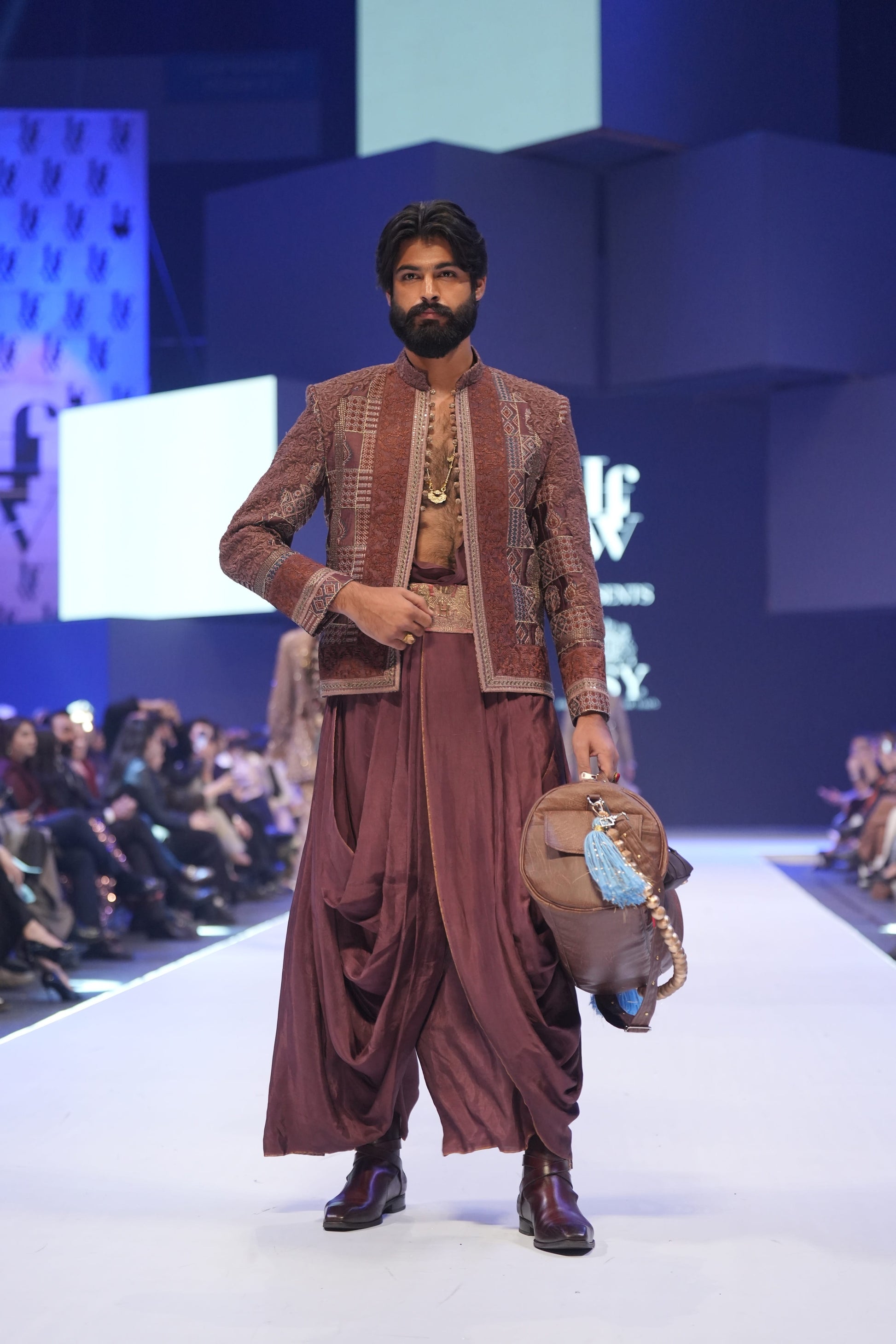 Model walking on a fashion show runway wearing a traditional outfit with a modern backdrop.
