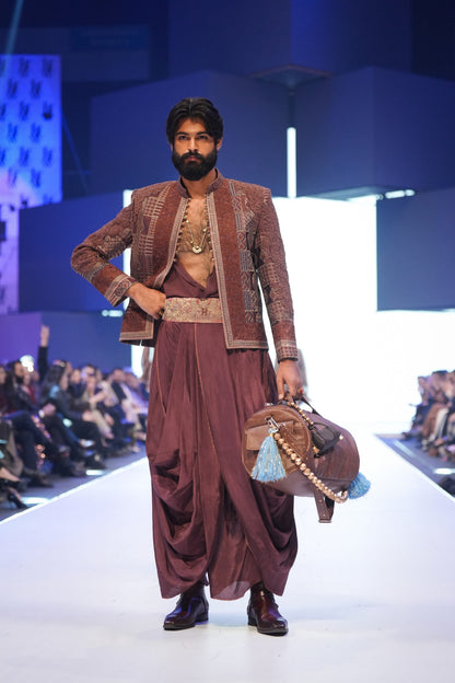 Man in traditional maroon outfit with a handbag on a runway