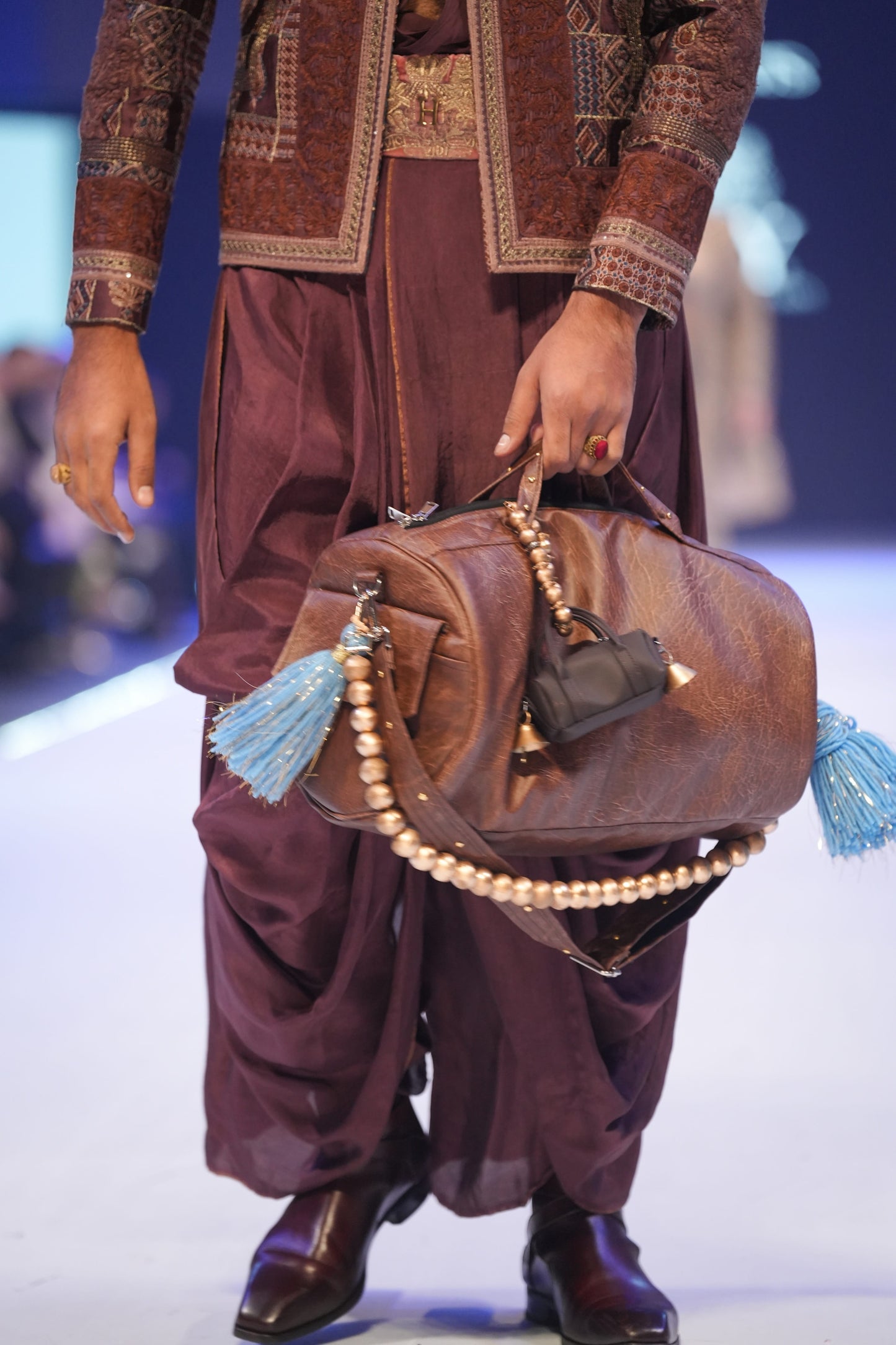 Person holding a brown leather bag with tassels on a runway