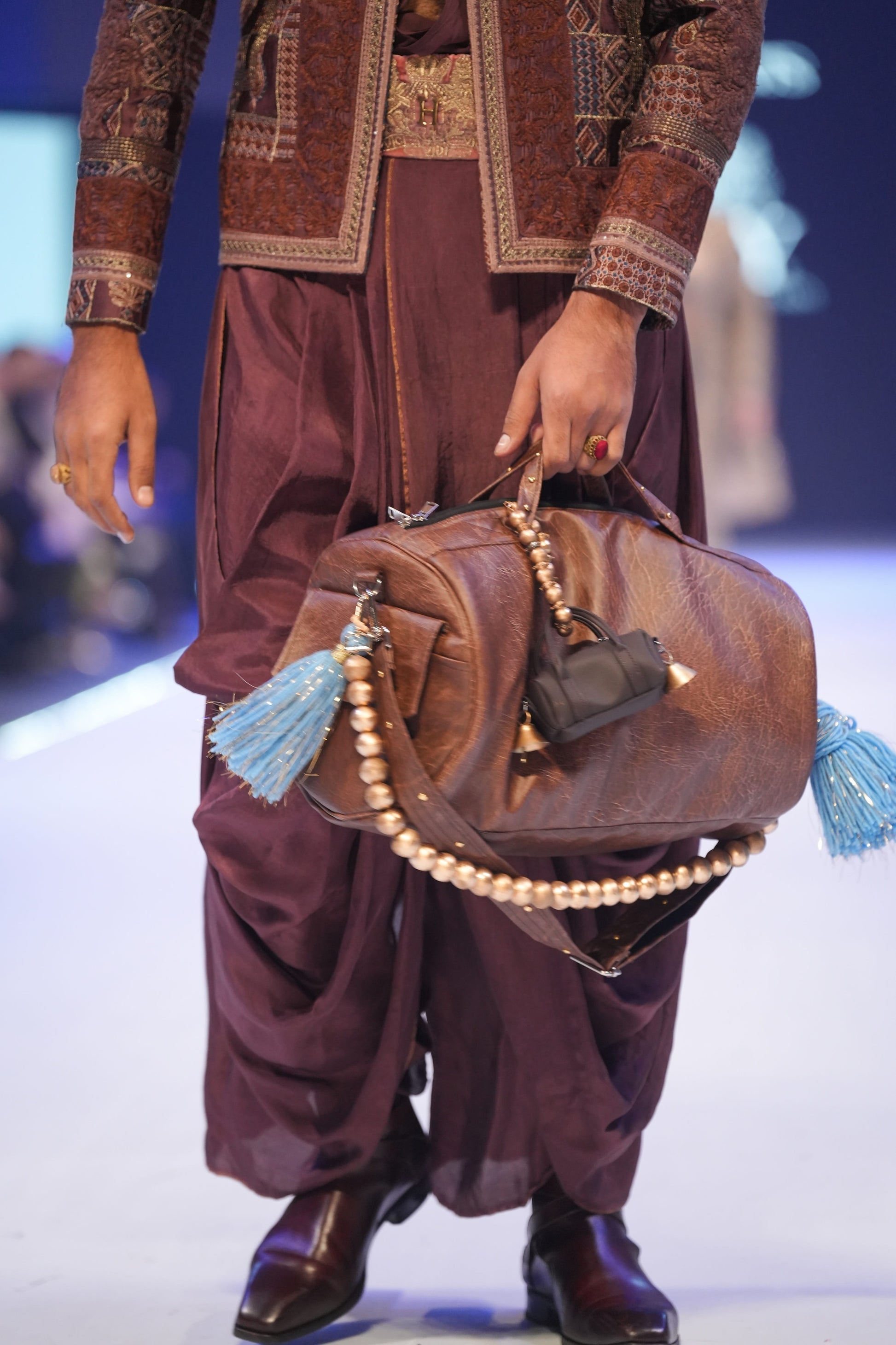 Person holding a brown leather bag with tassels on a runway