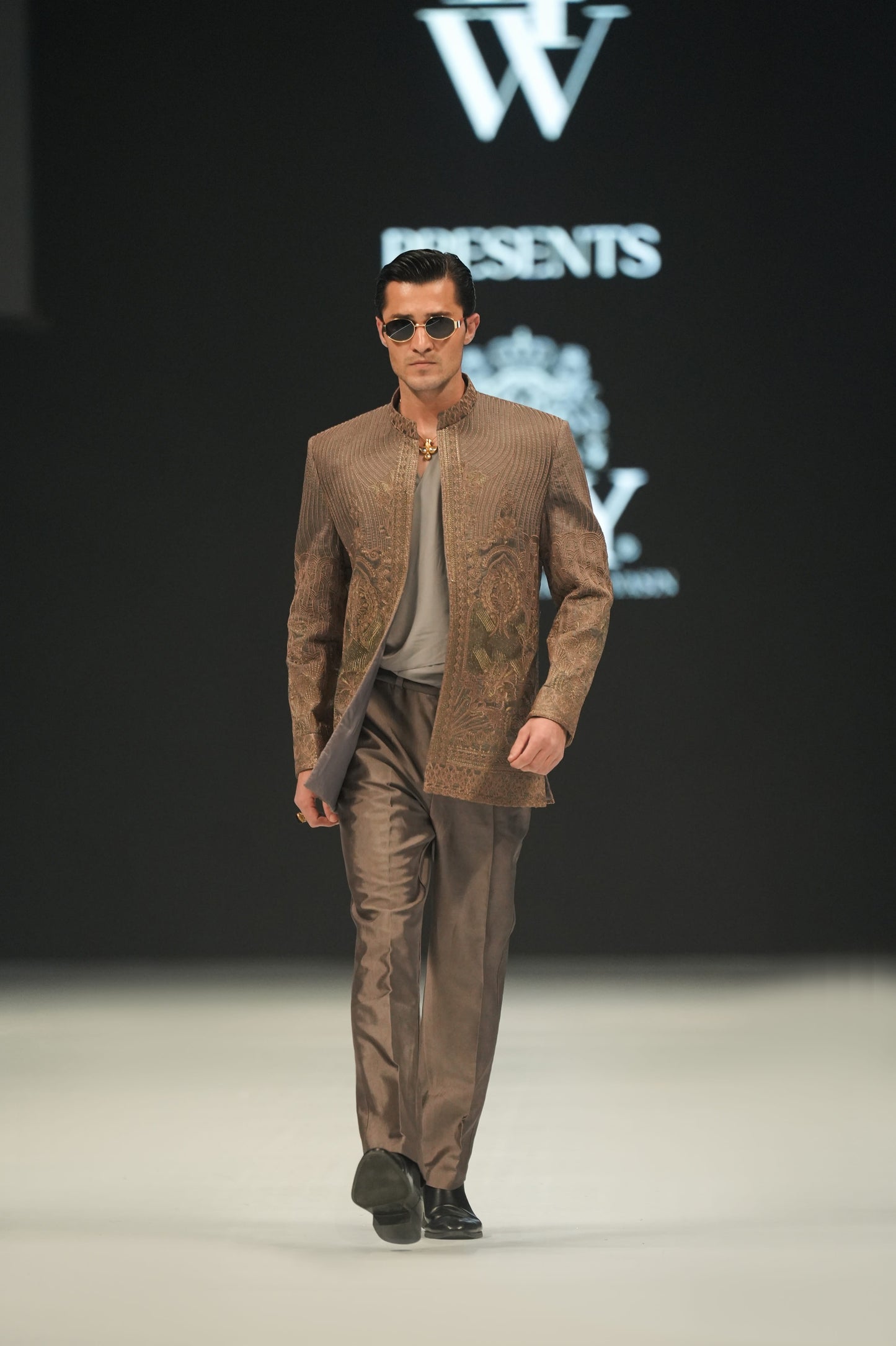 Man walking on a runway wearing a brown suit with sunglasses, against a black background with 'lfW' branding.