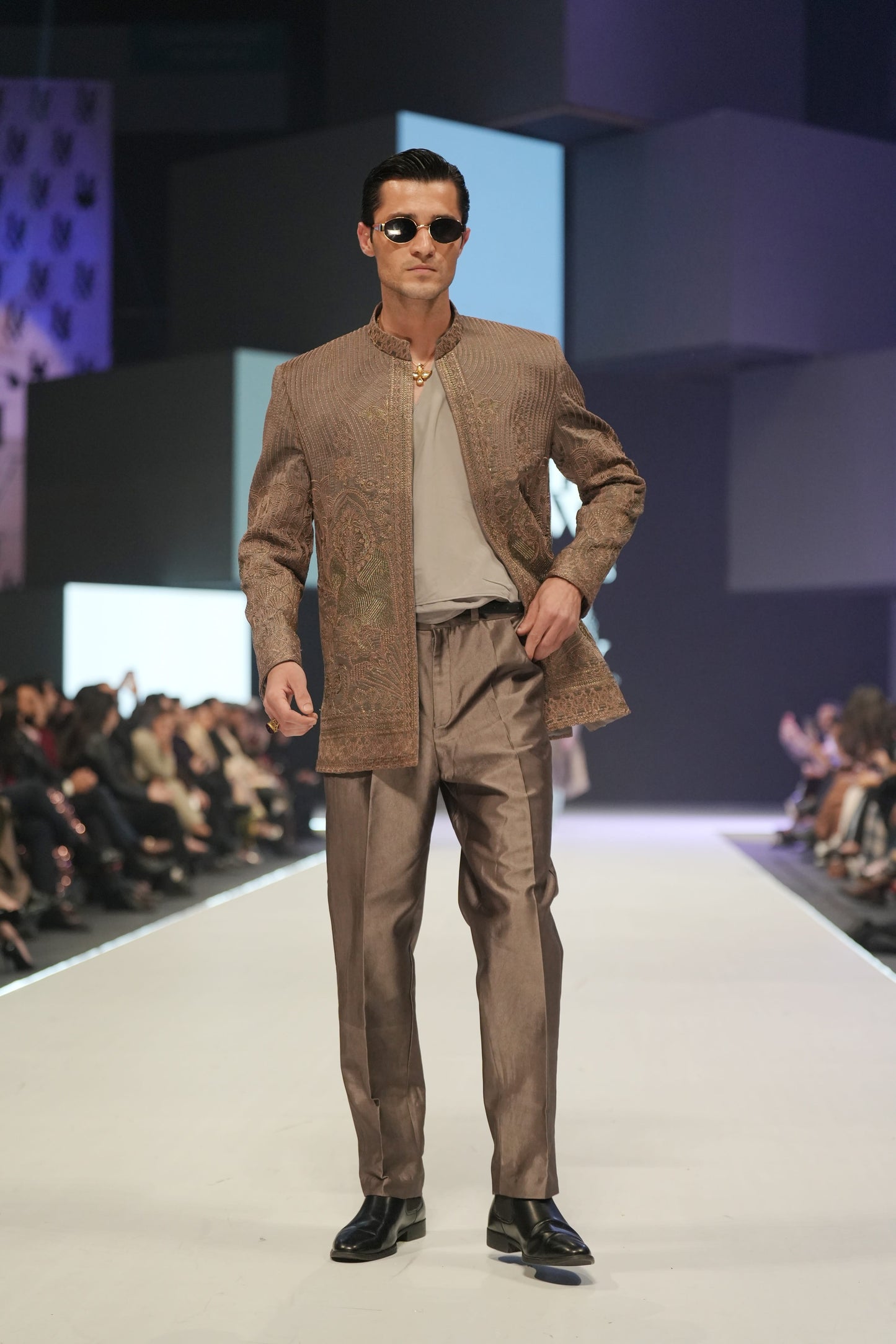 Man in a brown suit walking on a fashion show runway.