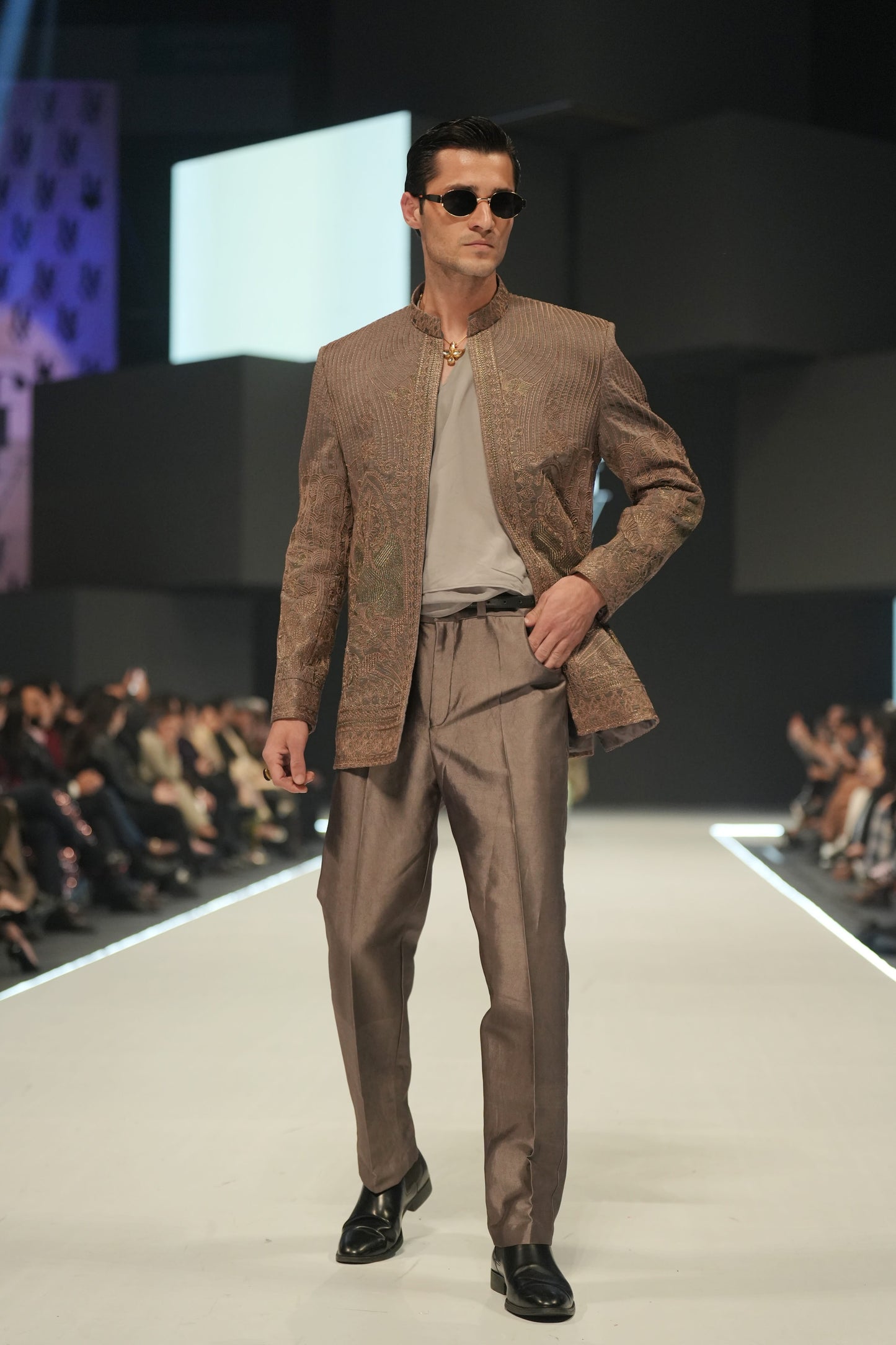 Man in a brown suit walking on a fashion show runway.