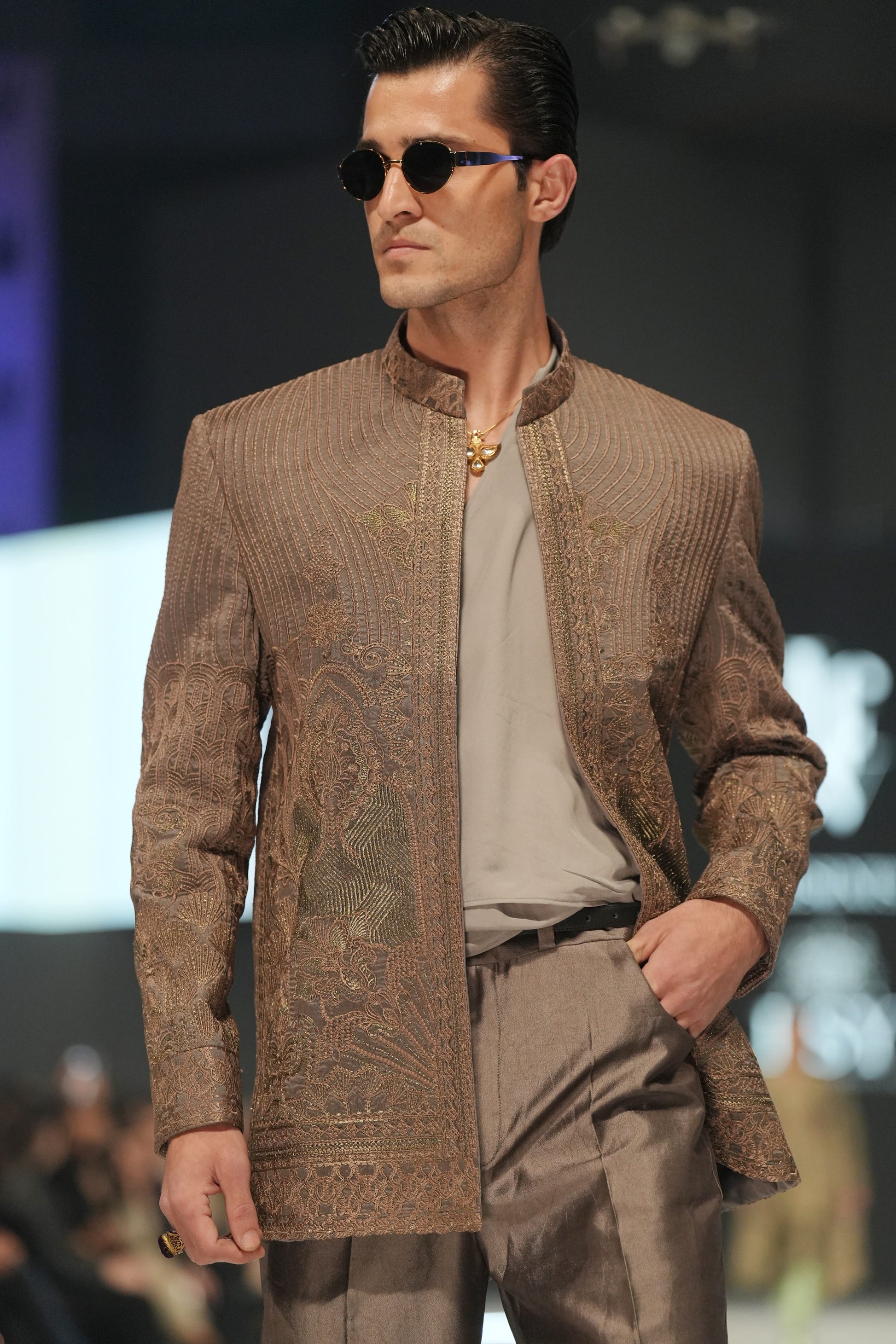 Man wearing a patterned brown jacket and sunglasses on a blurred background