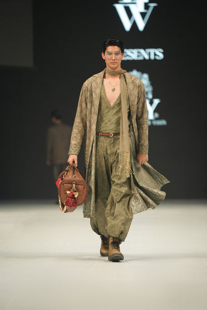 Model walking on a runway wearing a green outfit with a bag, with 'LFW' and 'HSY' logos in the background.