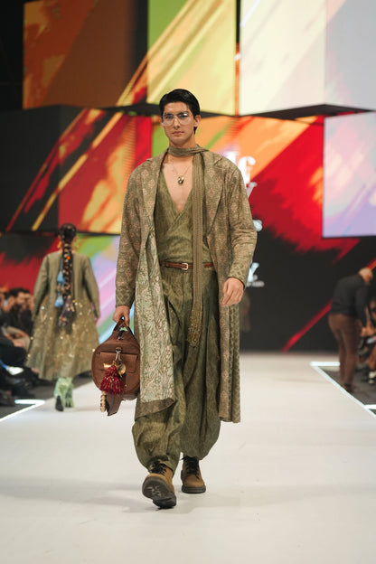 Model walking on a fashion show runway wearing a green outfit with a colorful abstract background.