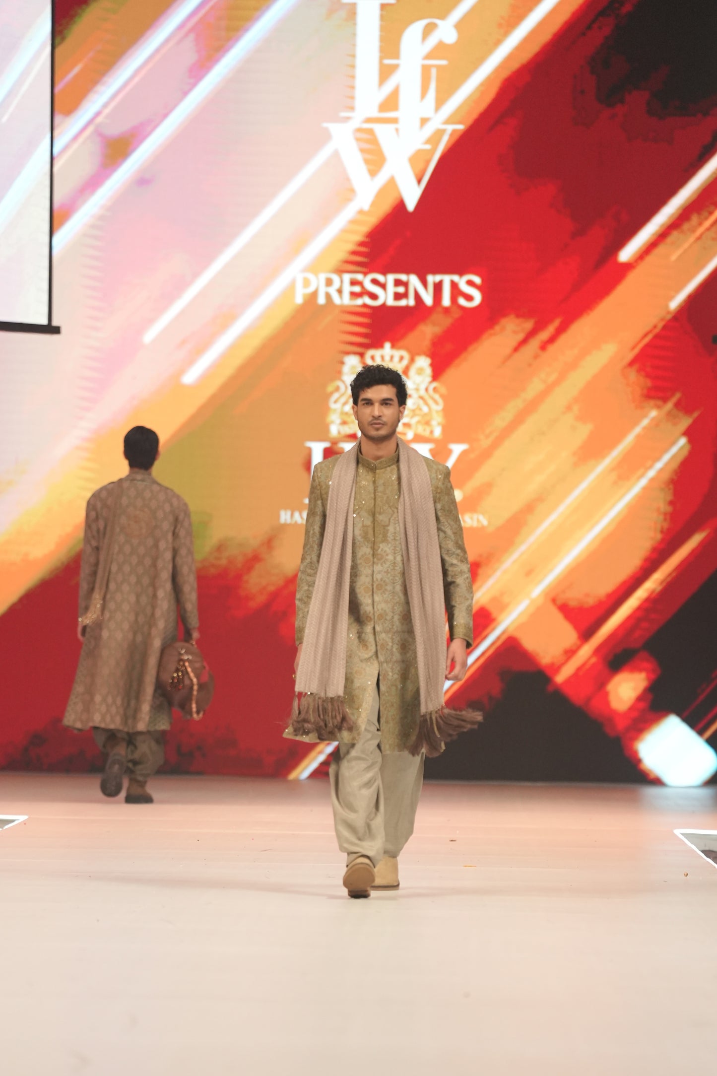 Two models walking on a catwalk with a vibrant, abstract background featuring the text 'LFW'.
