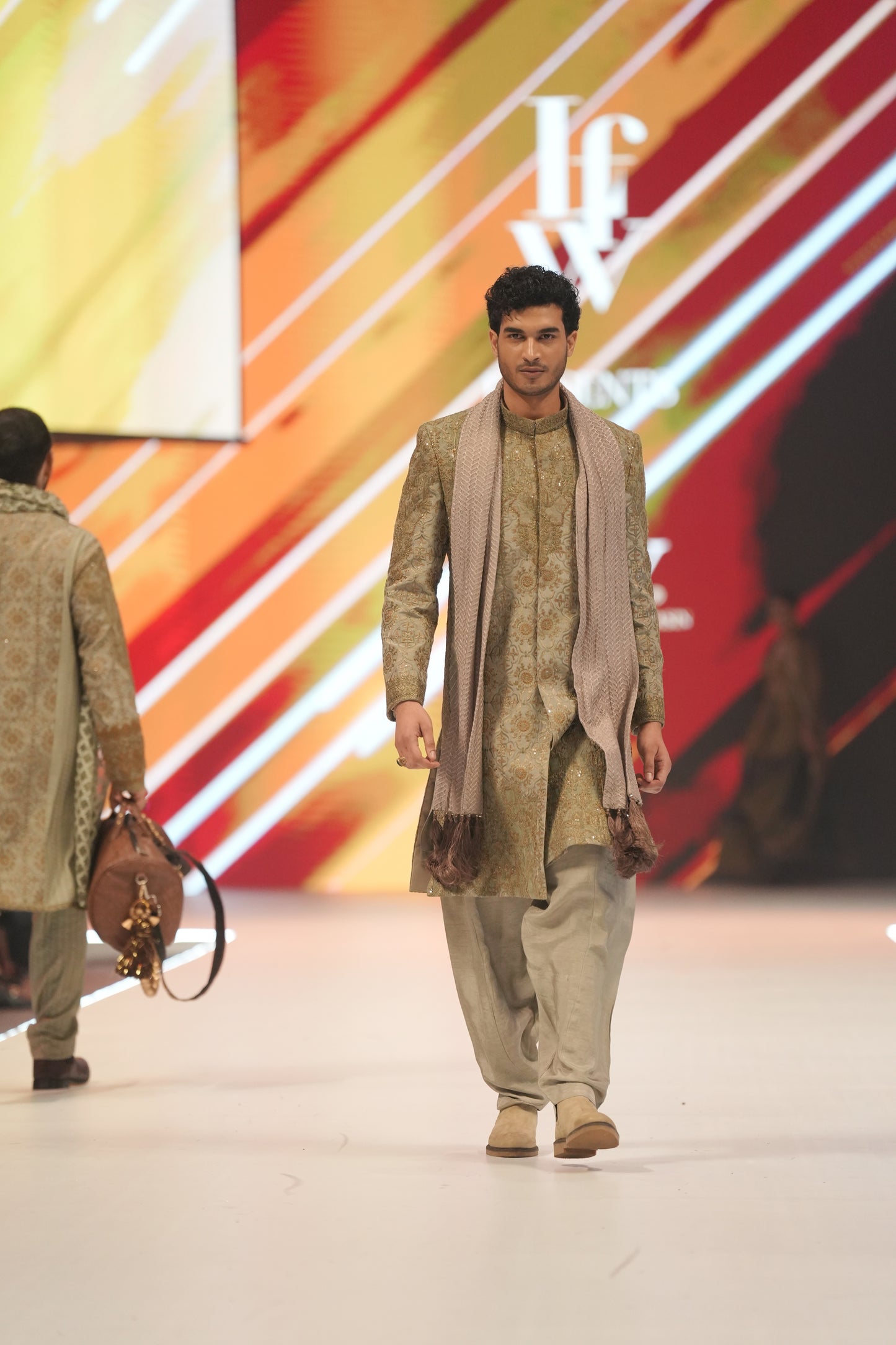 Man walking on a runway wearing a traditional outfit with a colorful background