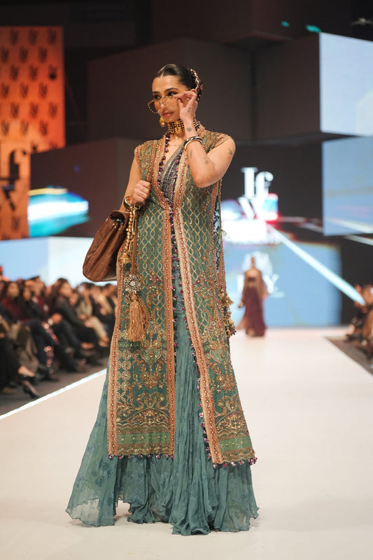 Model wearing a green embroidered outfit on a fashion show runway.
