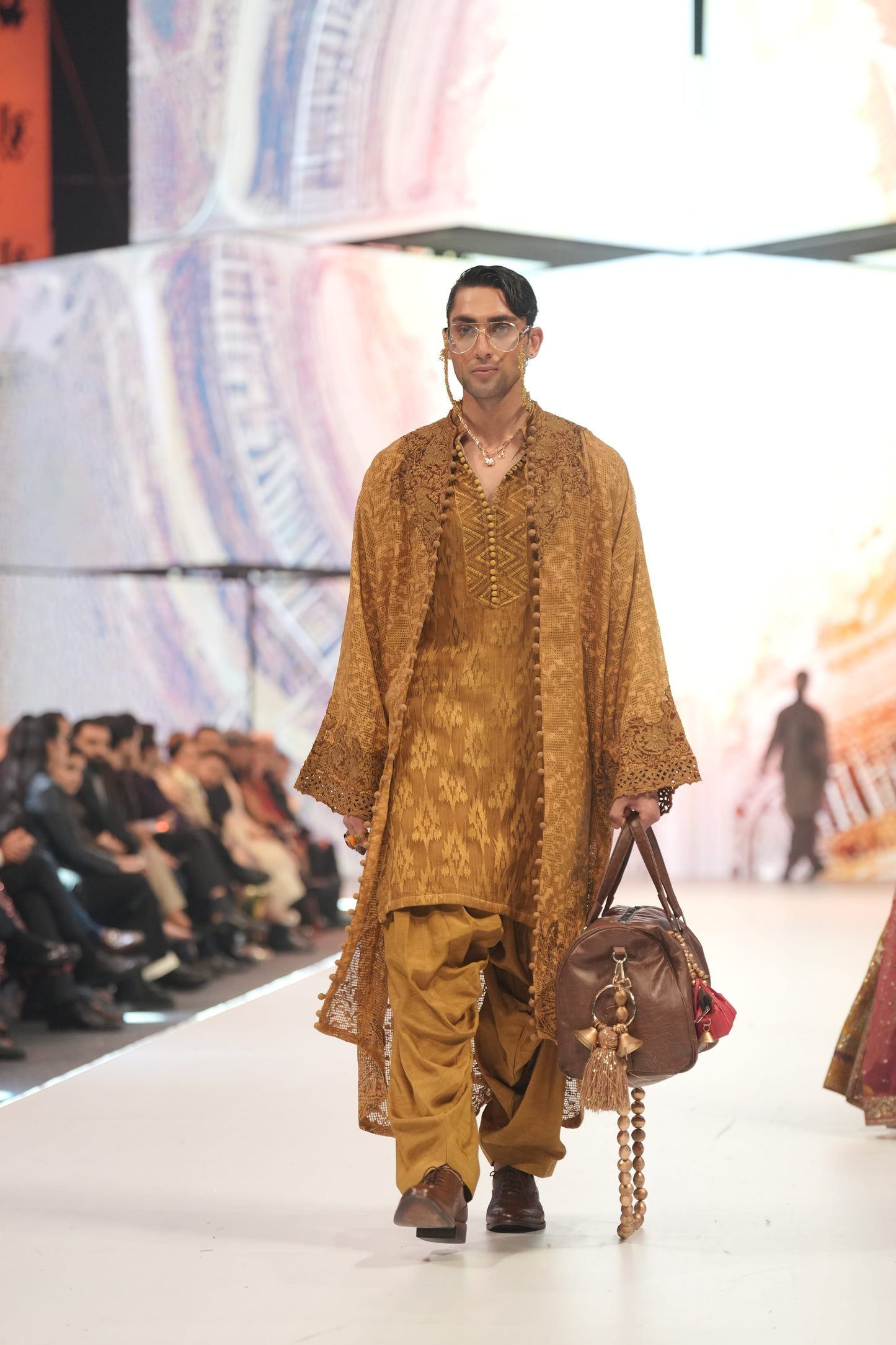 Man in a mustard yellow outfit walking on a fashion show runway with an audience.