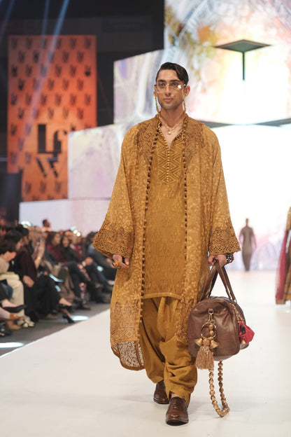 Man walking on a fashion show runway wearing a mustard yellow traditional outfit.