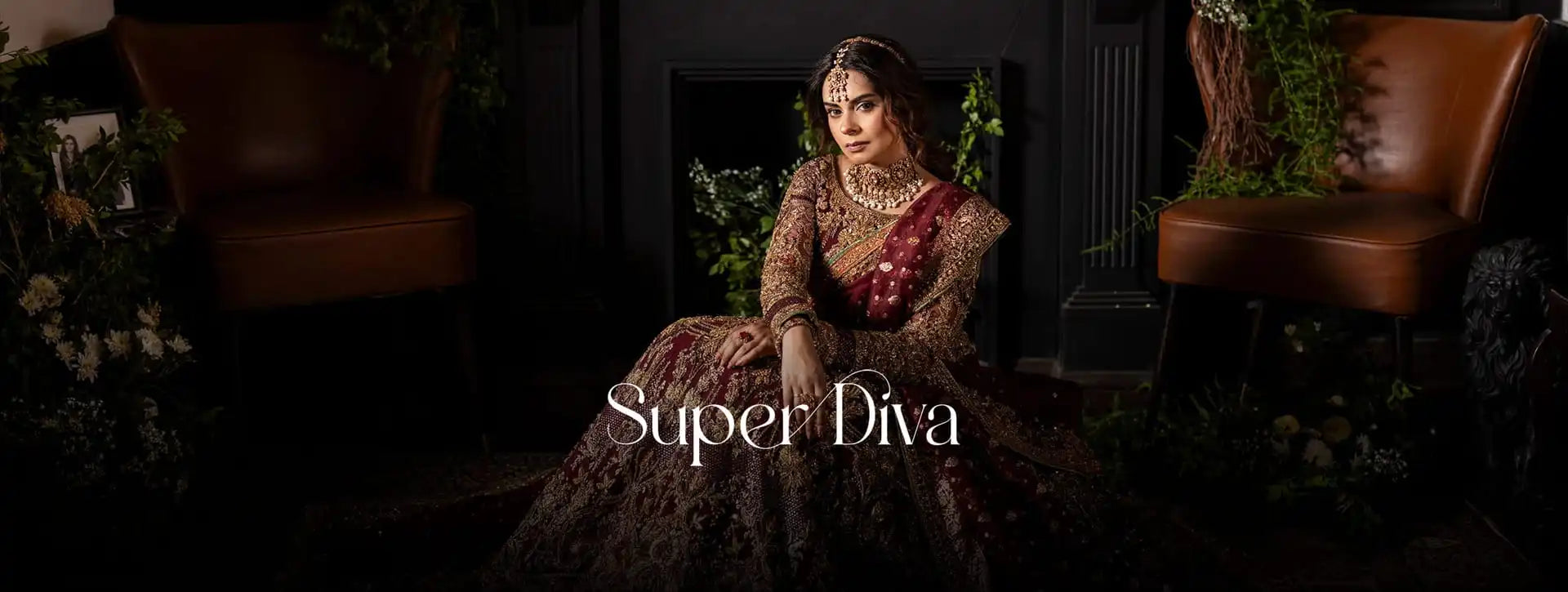 A woman wearing an ornate dark red and gold traditional gown sits in a dimly lit interior with brown chairs and greenery. The text 'Super Diva' appears across the lower center.
